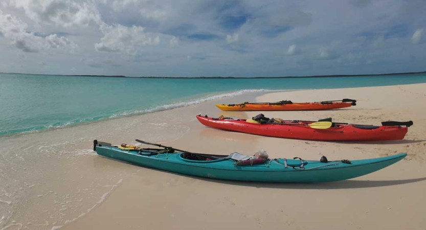 three empty kayaks rest on the white sand of a beach beside blue water